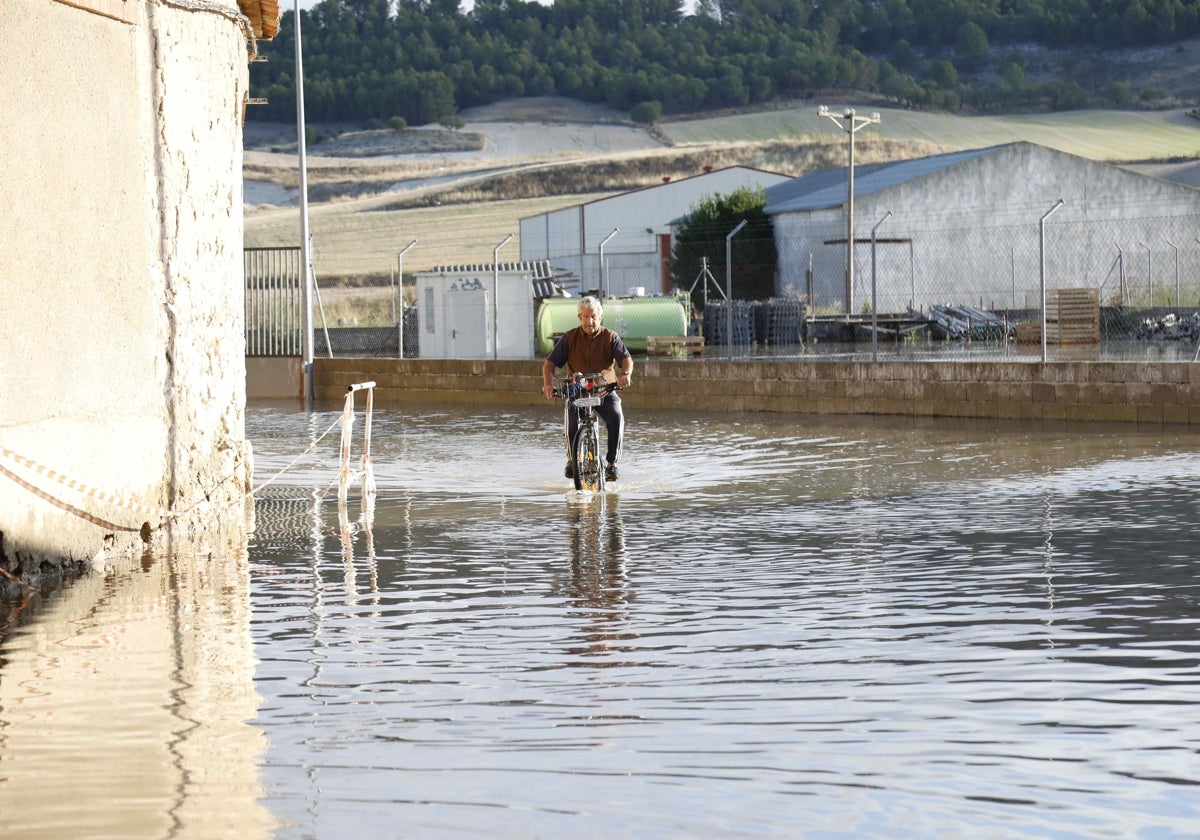 Un vecino de Valbuena transita en bicicleta por una de las calles anegadas por el reventón de la tubería del Canal del Riaza.