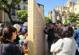 Varios segovianos observan la exposición en la Plaza Mayor de Segovia.