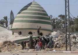 Palestinos desplazados esperan para llenar el tanque de agua cerca de edificios destruidos en Deir Al Balah, en el centro de la Franja de Gaza.