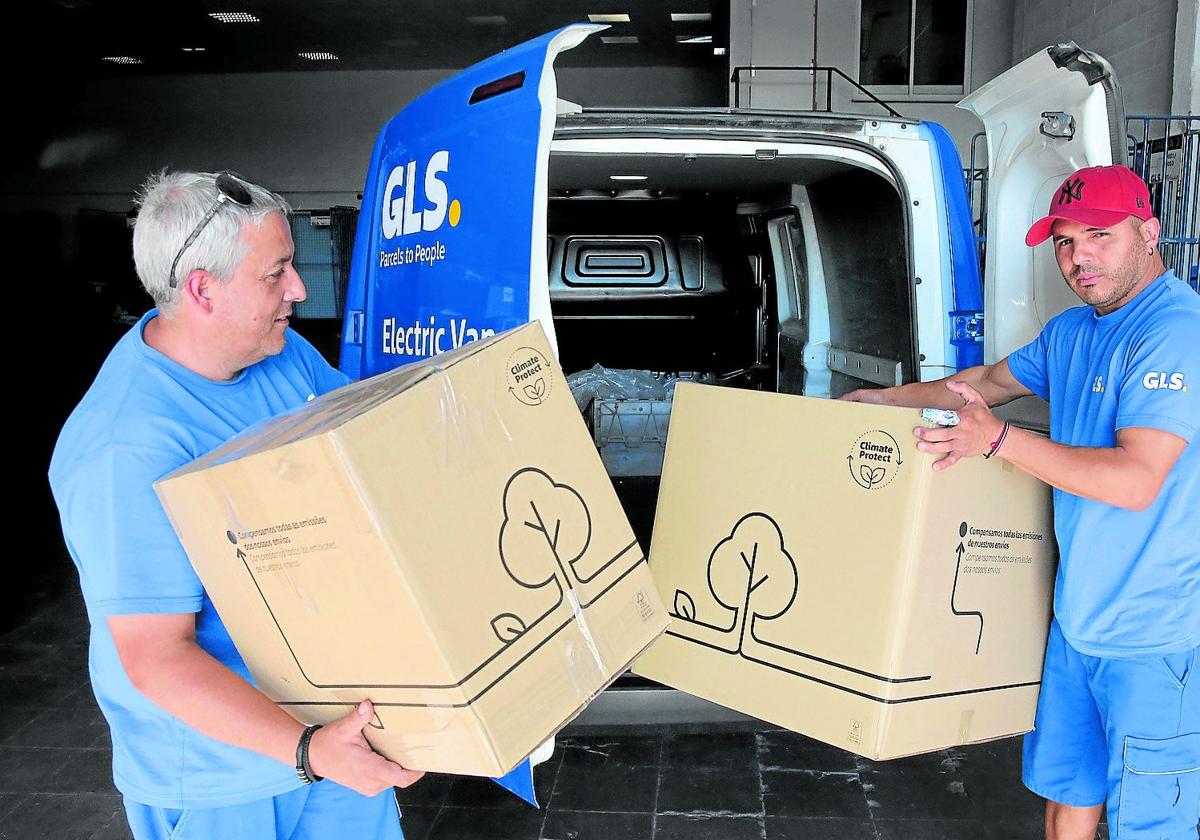 Dos repartidores descargan cajas de un vehículo eléctrico.