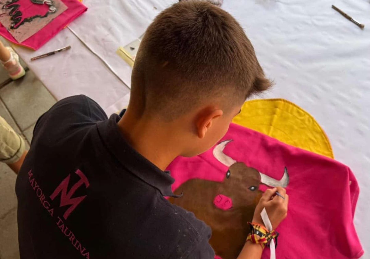 Un niño pinta un toro en su capote durante el taller