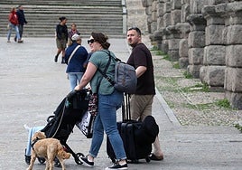 Dos turistas cruzan el Azoguejo con sus maletas.