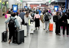 Varias personas esperan la salida de su tren en la estación de Atocha en Madrid este domingo.