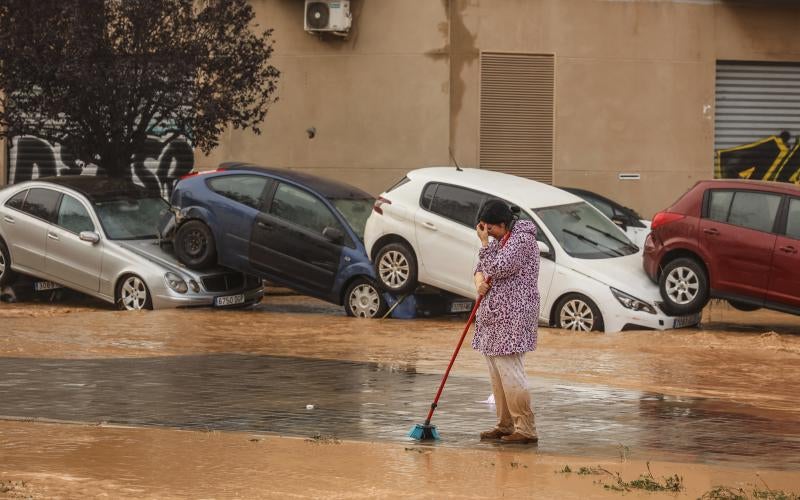 Una mujer realiza labores de limpieza junto a vehículos destrozados tras el paso de la DANA por el barrio de La Torre de Valencia.