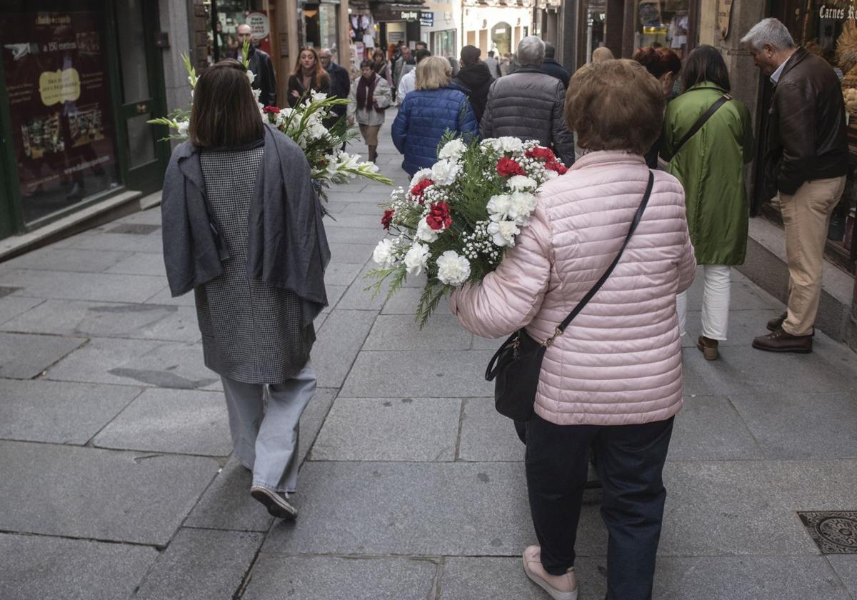 Dos mujeres abrigadas portan arreglos florales recién comprados.