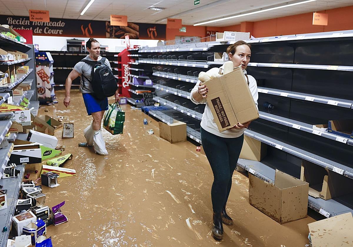 Dos personas recogen alimentos en un supermercado casi vacío de la localidad valenciana de Paiporta.