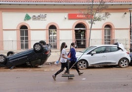 Dos mujeres pasan frente a vehículos dañados en Aldaya.