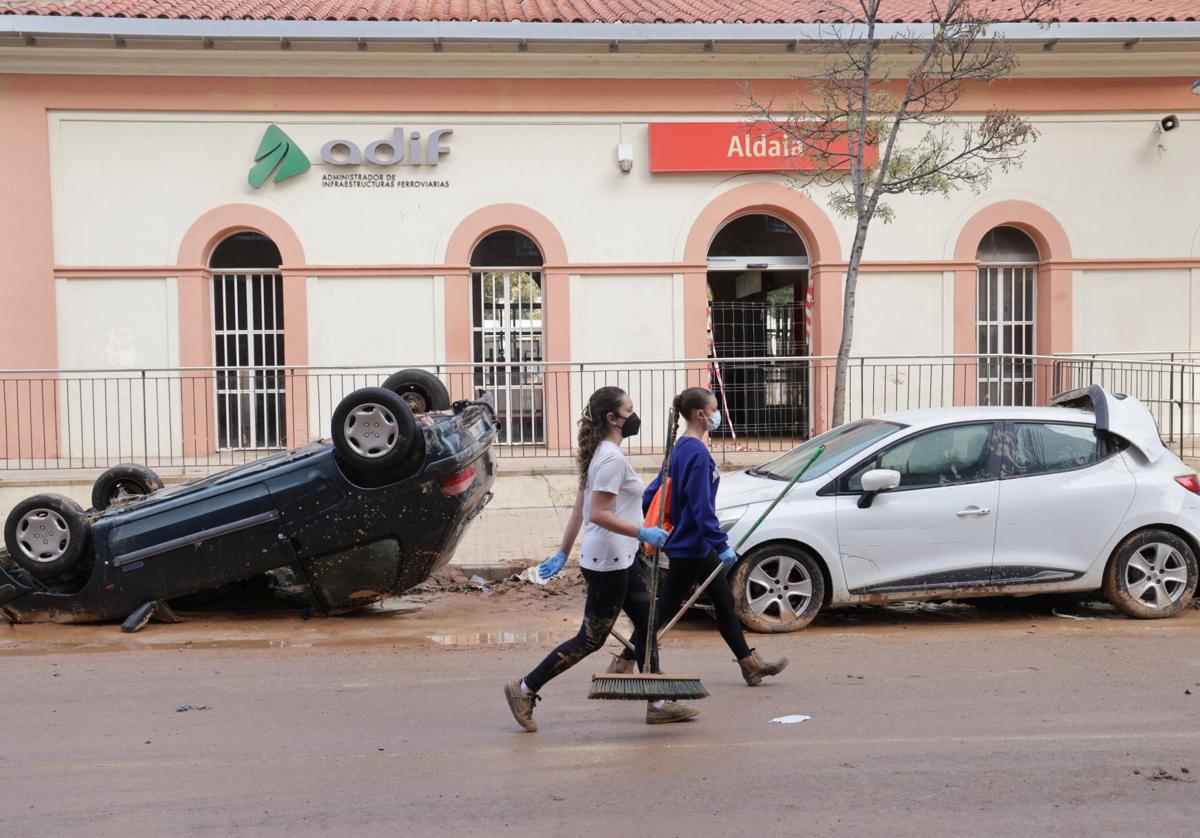 Dos mujeres pasan frente a vehículos dañados en Aldaya.