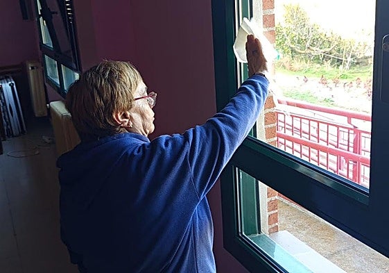Una de las participantes en el proyecto social limpia un cristal en un edificio.