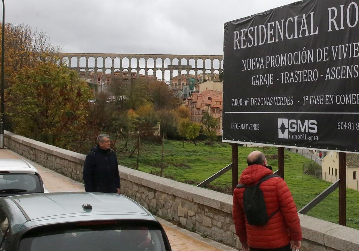 Un hombre observa un cartel colocado junto a los terrenos en los que se construirá la promoción de viviendas.