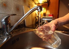 Un hombre recoge agua en un vaso de un grifo.