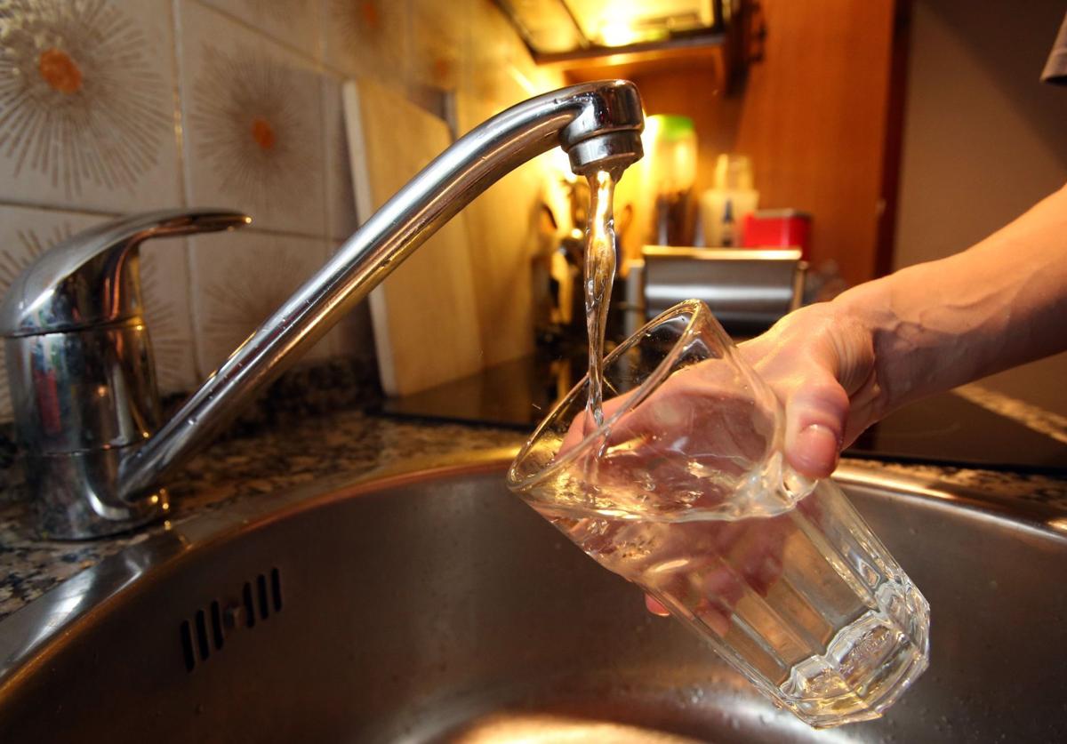 Un hombre recoge agua en un vaso de un grifo.