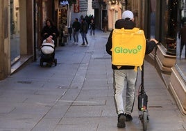 Un repartidor lleva el patinete de la mano por la Calle Real de Segovia, que es peatonal.