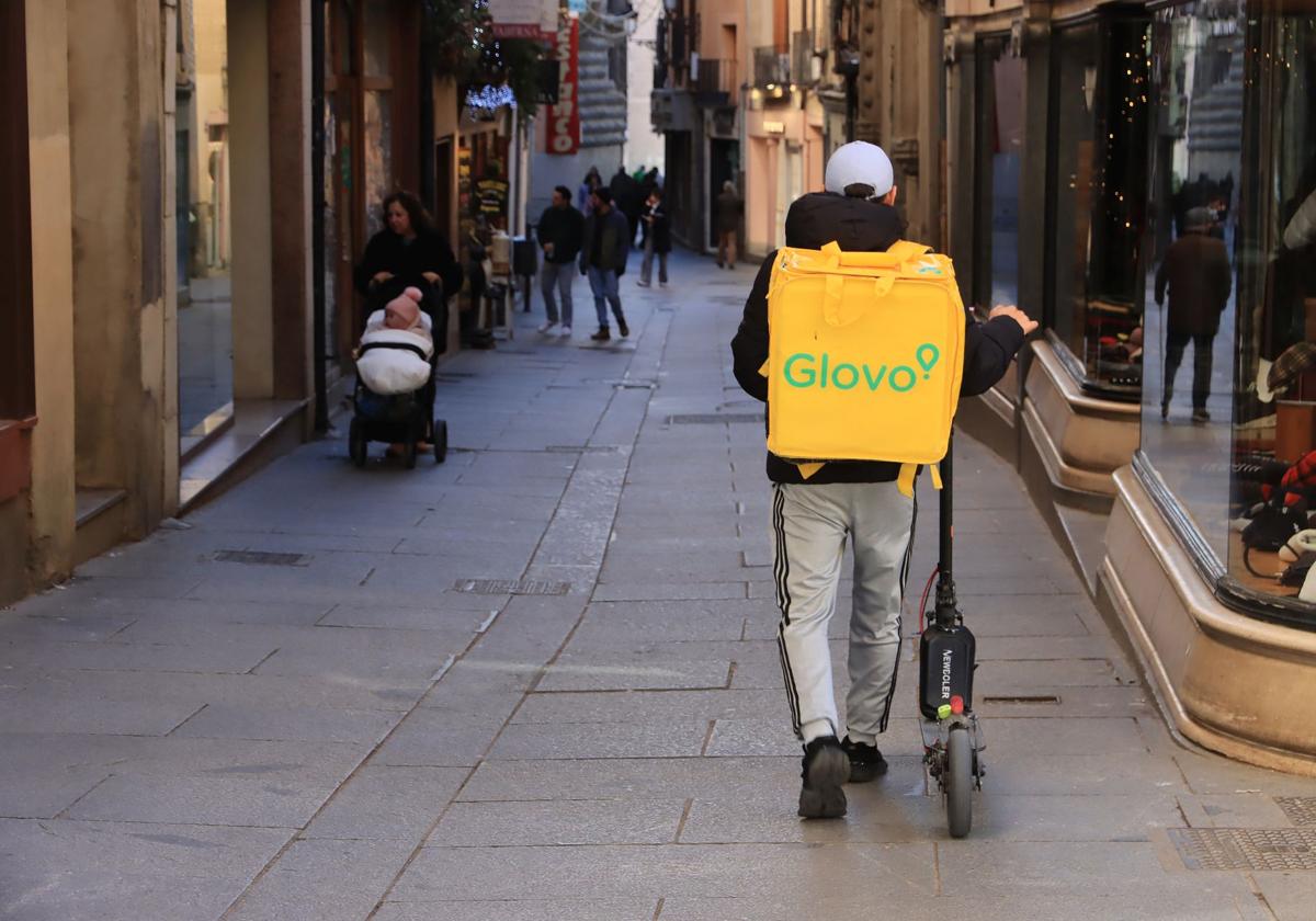 Un repartidor lleva el patinete de la mano por la Calle Real de Segovia, que es peatonal.