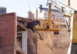 Un operario con una larga vara retira los elementos con más riesgo de caída de la parte superior del edificio.