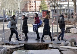 Varios peatones caminan por encima de una placa que salva una de las zanjas de la red de calor en Valladolid.