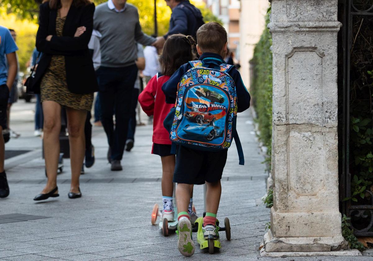 Dos niños, a bordo de un patinete, acuden a clase en un colegio del centro de Valladolid.