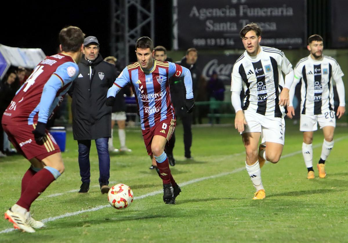 Manu conduce el balón durante el partido en Tarazona ante la mirada de Ramsés desde la banda.