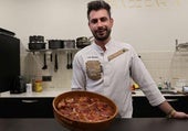 El cocinero Laín Montes posa con una cazuela de barro llena de sopas de ajo con costra recién hechas.