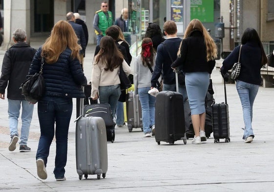 Varias personas caminan con maletas por una calle de la ciudad de Segovia.