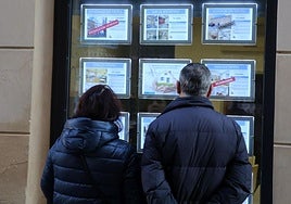 Dos personas observan la oferta de viviendas a la venta en una inmobiliaria de Segovia.
