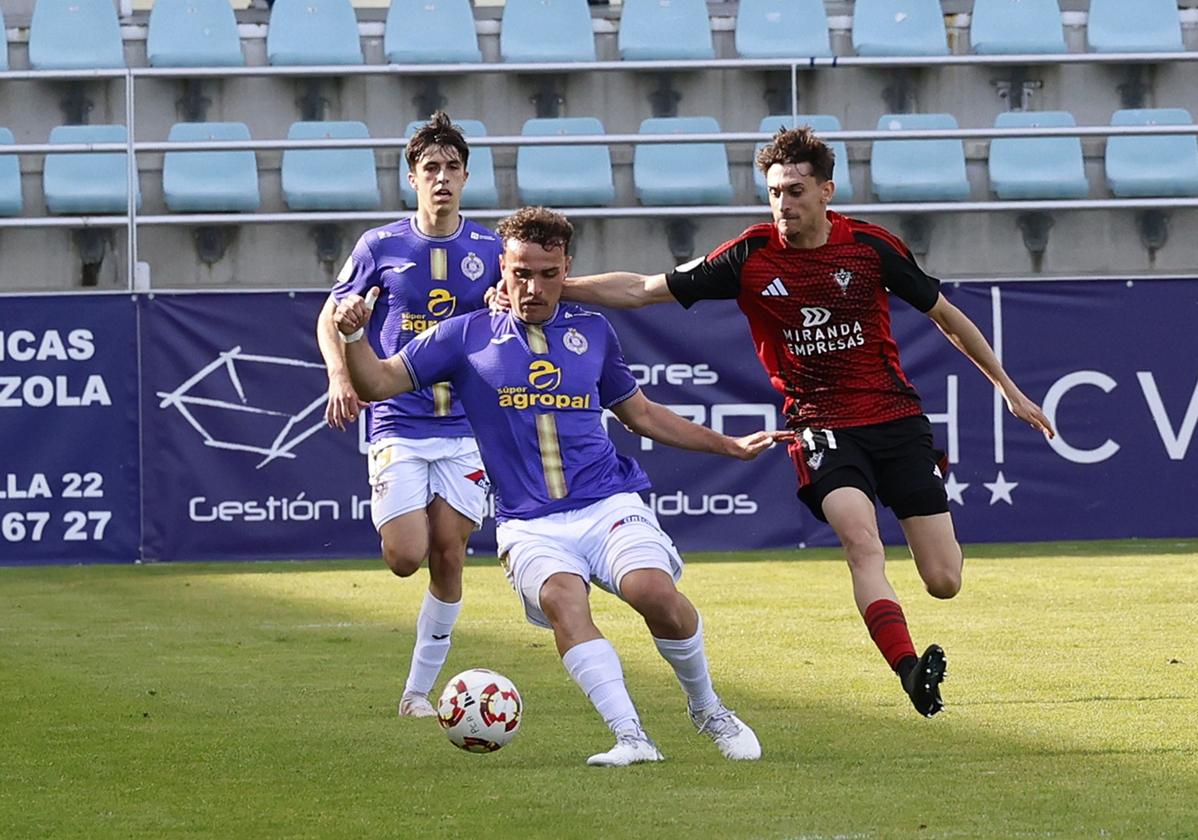Javi Romano intenta progresar con el balón agarrado por un rival.