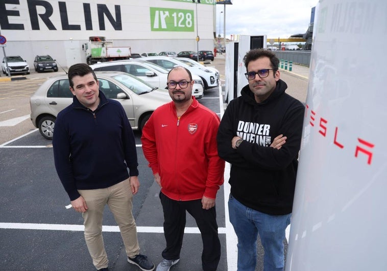 Laurentino Gutiérrez, Alberto Muñoz y Pablo Gutiérrez, miembros de la Asociación de Usuarios de Vehículos Eléctricos de Castilla y León, posan junto a un cargador de Tesla. Al fondo, coches de combustión ocupan las plazas de forma indebida.