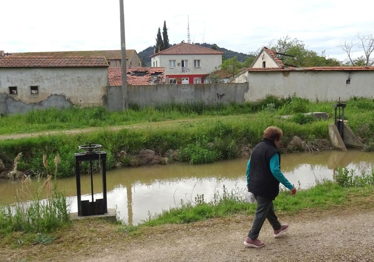 Una mujer pasea por el camino del Canal del Duero que discurre por el lateral de la Granja Luisa, en el polígono de San Cristóbal, donde se asoma la casa ocupada en el terreno municipal desde hace seis años.