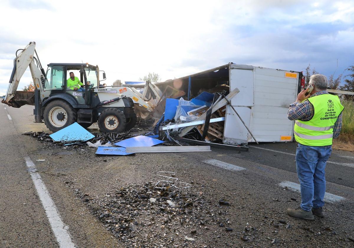 Una excavadora retira la carga del camión volcado en la carretera.