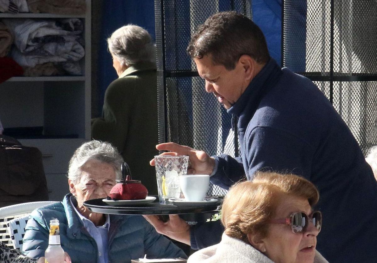 Un hostelero de origen latinoamericano sirve a unas clientas en una terraza de un bar.