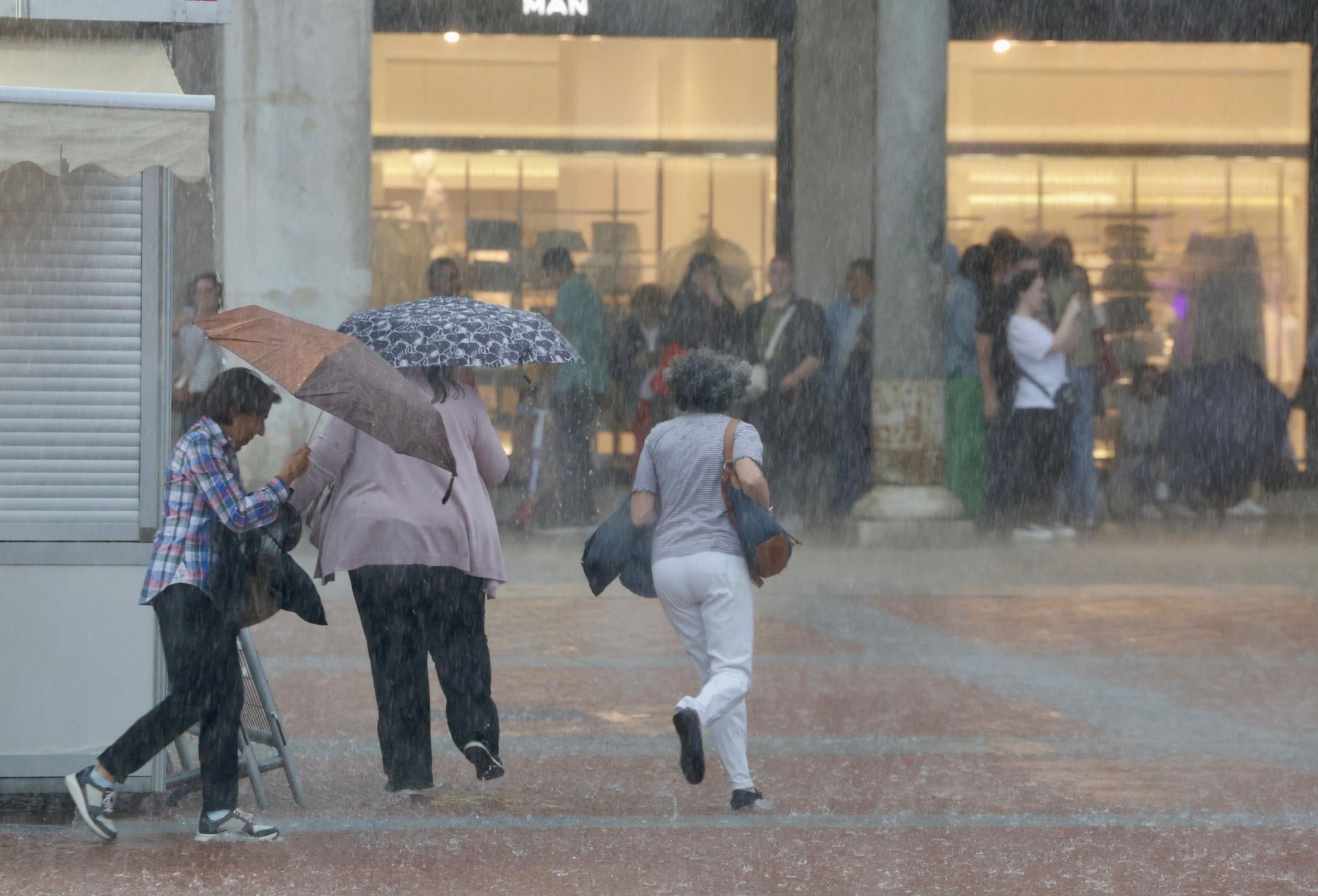 Varias personas corren a refugiarse en los soportales de la Plaza Mayor.