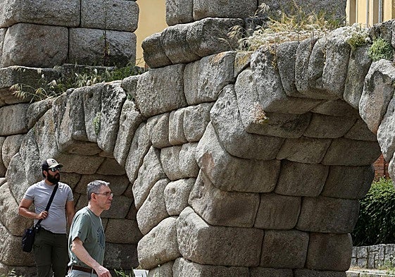 Dos hombres pasean junto a dos arcos del Acueducto con abundante vegetación.