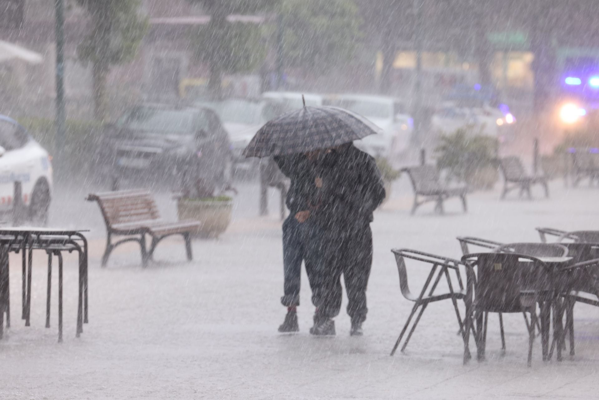 Dos personas intentan refugiarse de la tormenta bajo un paraguas.