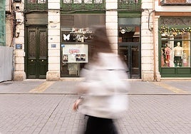 Una joven camina en la calle Platerías de Valladolid por delante de un negocio cerrado.