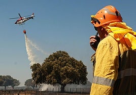 Tres hombres observan cómo un helicóptero vierte agua para refrescar un terreno recién arrasado por un incendio forestal.