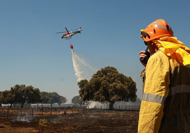 Un helicóptero del operativo contra incendios descarga agua sobre terreno quemado.