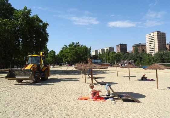 Las máquinas esparcen la arena por la playa de Las Moreras mientras dos usuarios toman el sol en el mobiliario estrenado el pasado verano.