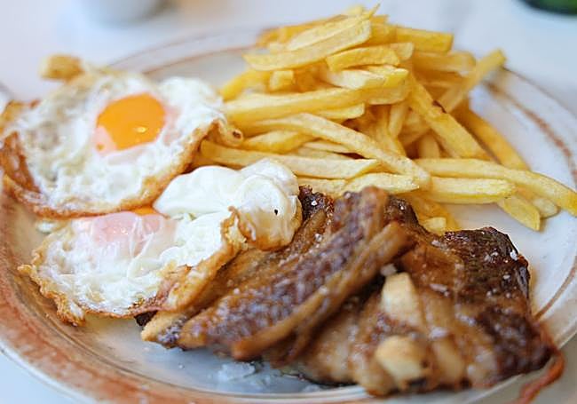Segundo plato del menú, churrasco de ternera con dos huevos y patatas.