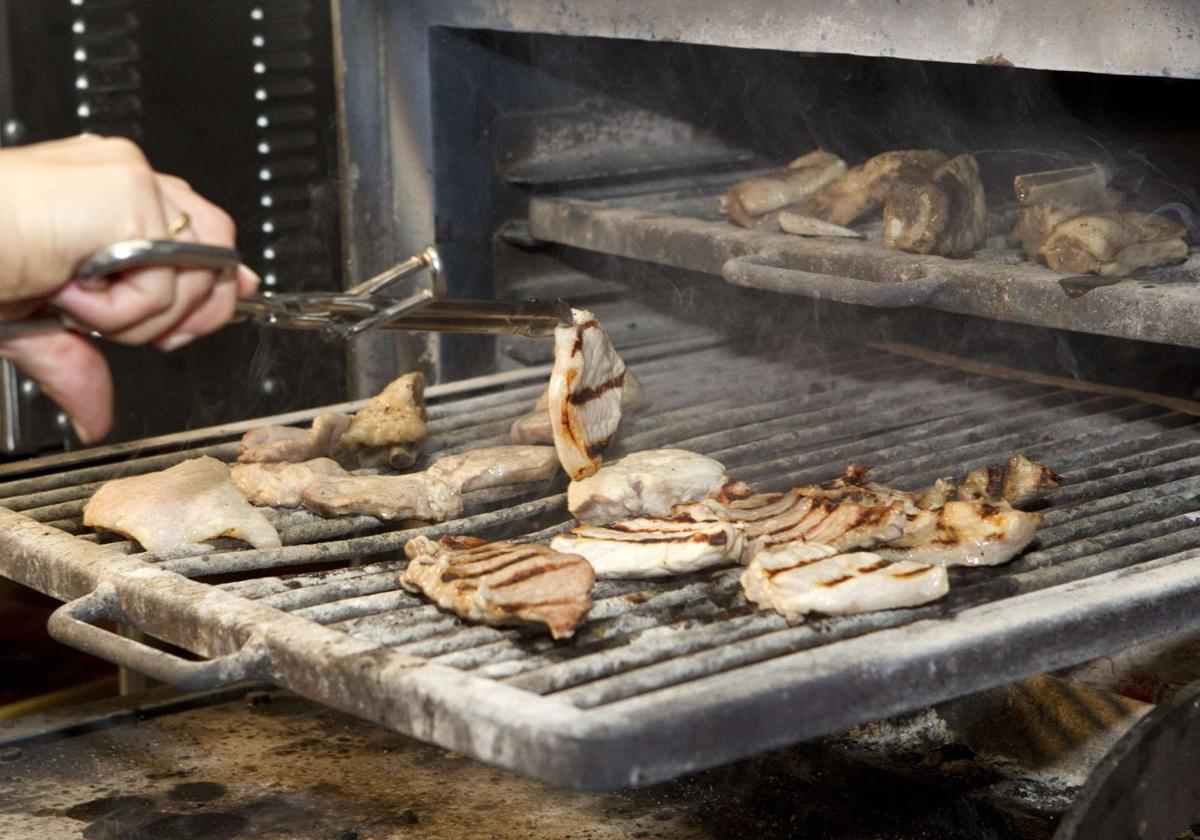 Una persona da la vuelta a la carne en una parrilla en una imagen de archivo.