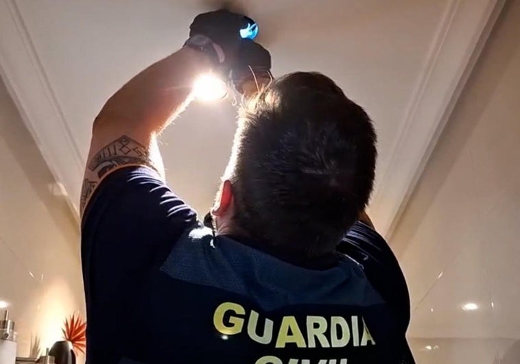 Un agente de la Guardia Civil retira la cámara que el detenido tenía escondida en un foco del techo de su baño y con la que grababa a familiares y amigos sin su consentimiento.