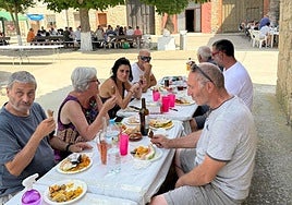 Los vecinos comen en grupos a la sombra, en la paella solidaria de Cordovilla la Real.