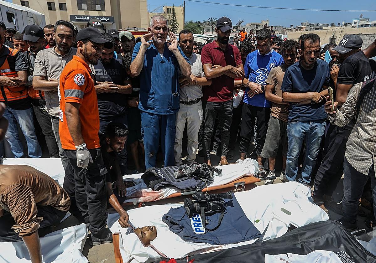 Un grupo de palestinos junto a los cadáveres de dos de los periodistas asesinados ayer en el ataque contra el hospital Nasser de Gaza.