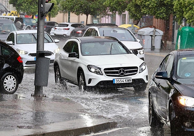 Los coches pasan por una balsa de agua generada por la tormenta en la calle Puente Colgante.