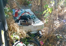 Un indigente duerme en un colchón, rodeado de basura, en la ribera del río frente al albergue municipal del paseo de Extremadura.