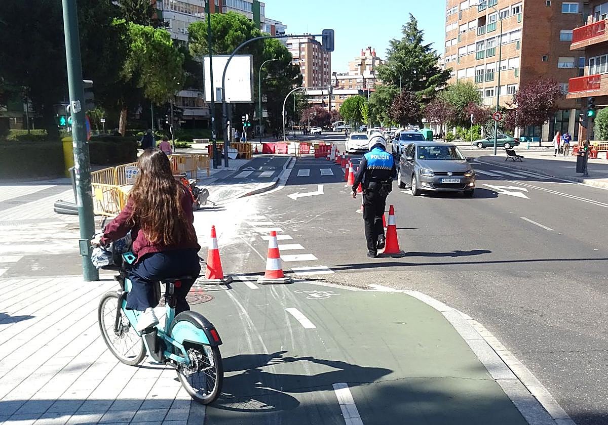 Un agente supervisa los conos del carril de giro de la avenida de Gloria Fuertes hacia la calle Arzobispo José Delicado, cortada al tráfico, antes del puente de Poniente, mientras una ciclista se topa con carril bici cerrado.