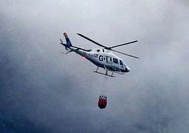 Un helicóptero esparce agua, este lunes, sobre los puntos calientes del incendio de Cerezo de Arriba volando entre el humo y las nubes.