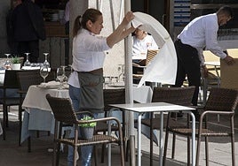 Una camarera extiende un mantel en una mesa de una terraza de la capital segoviana.