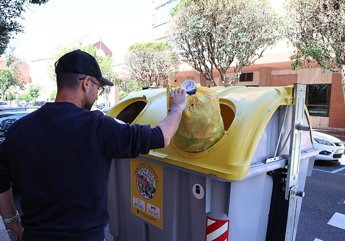 Un hombre tira una bolsa de basura en el contenedor amarillo.