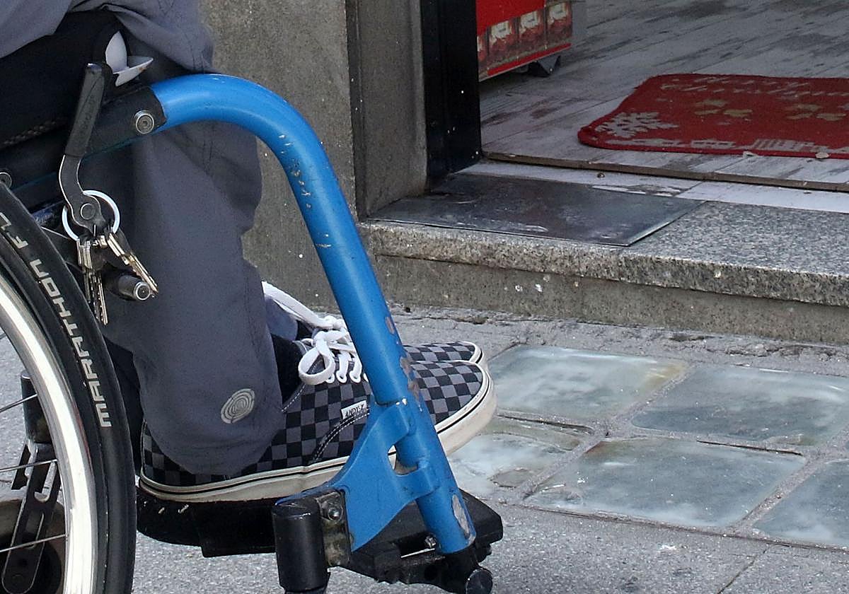 Una persona en silla de ruedas justo en el acceso a un inmueble donde hay un escalón.