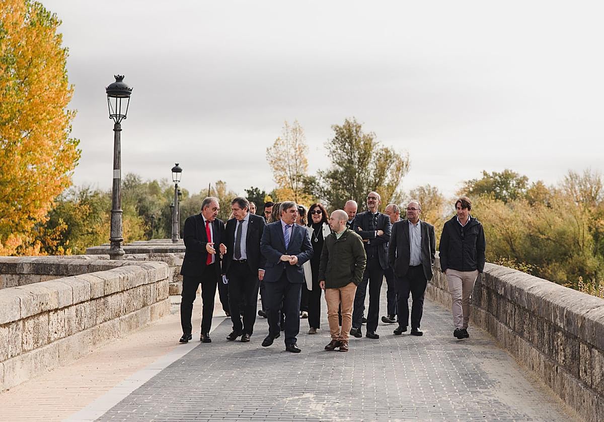 El consejero y el alcalde de Villamuriel, en primer término, pasean por el renovado puente sobre el río Carrión.